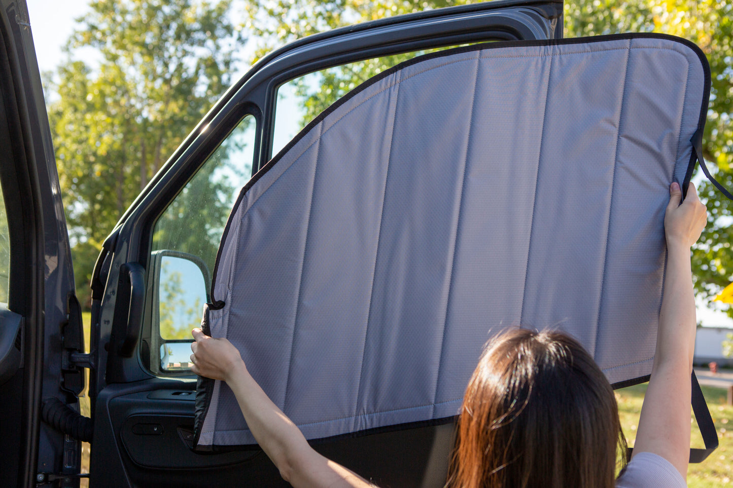 Image of a person attaching a cover to the passenger side window for a Sprinter van, demonstrating the installation process.