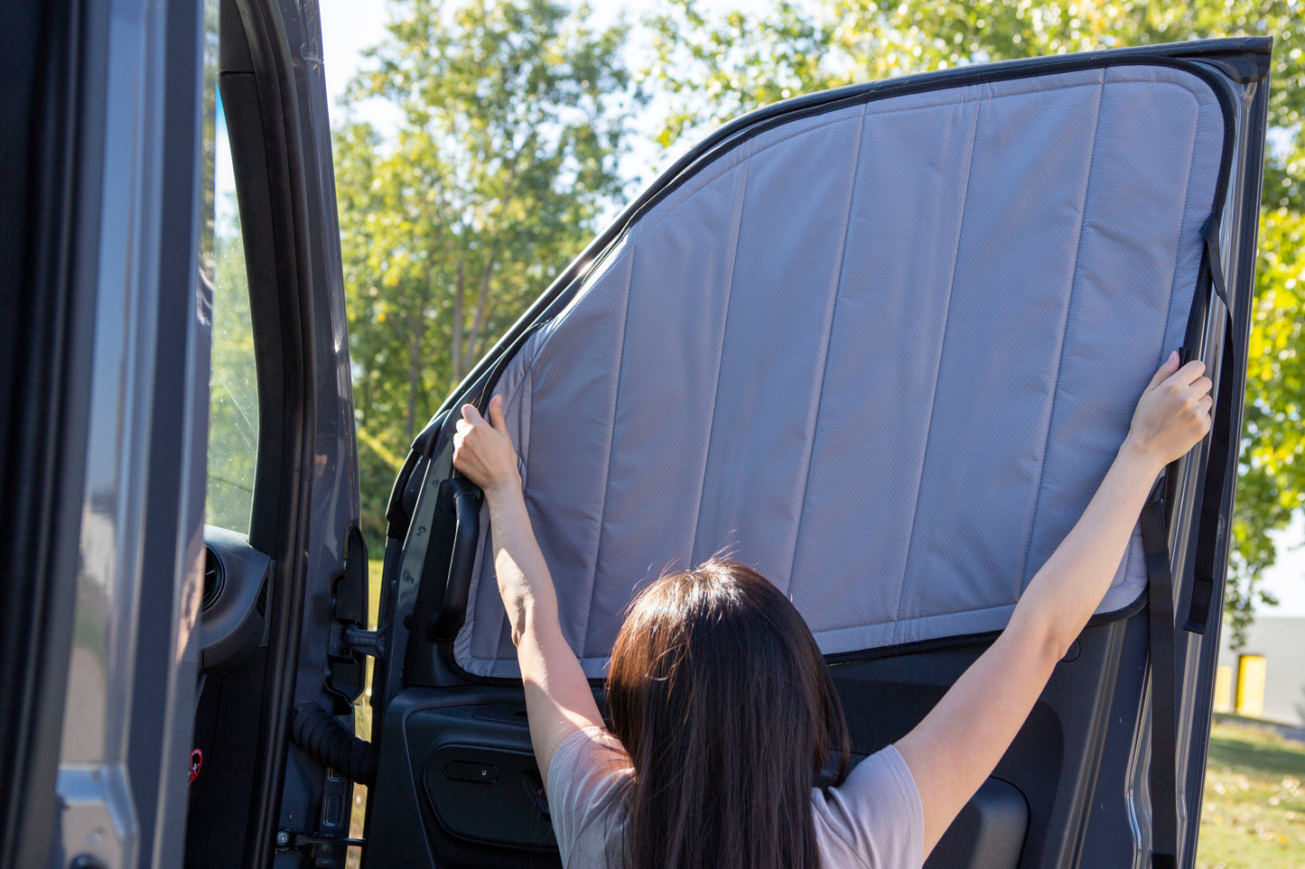 Image of a person attaching a cover to the passenger side window for a Sprinter van, demonstrating the installation process.