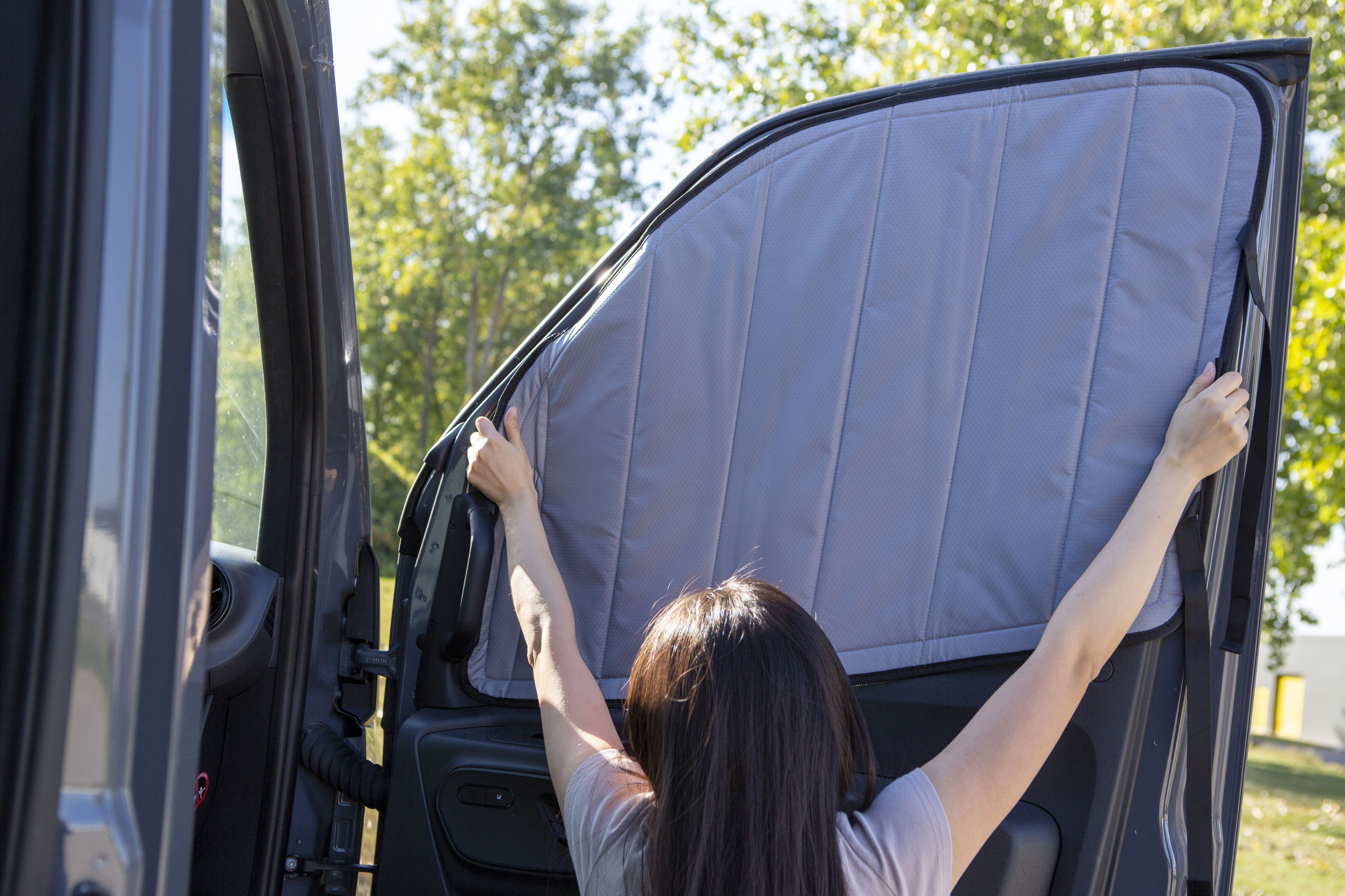 Image of a person attaching a cover to the passenger side window for a Sprinter van, demonstrating the installation process.