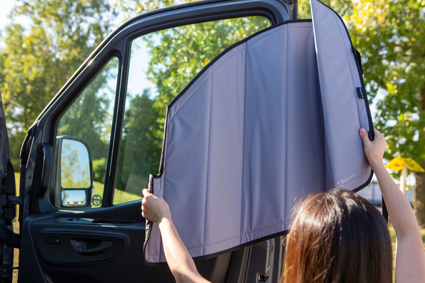 Image of a person attaching a cover to the passenger side window for a Sprinter van, demonstrating the installation process.