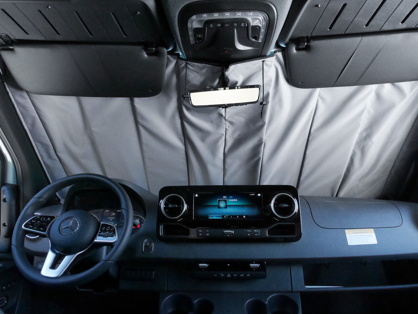 Image showing the window cover for the windshield securely tucked behind the rearview mirror in a Sprinter van, demonstrating a snug and seamless fit.