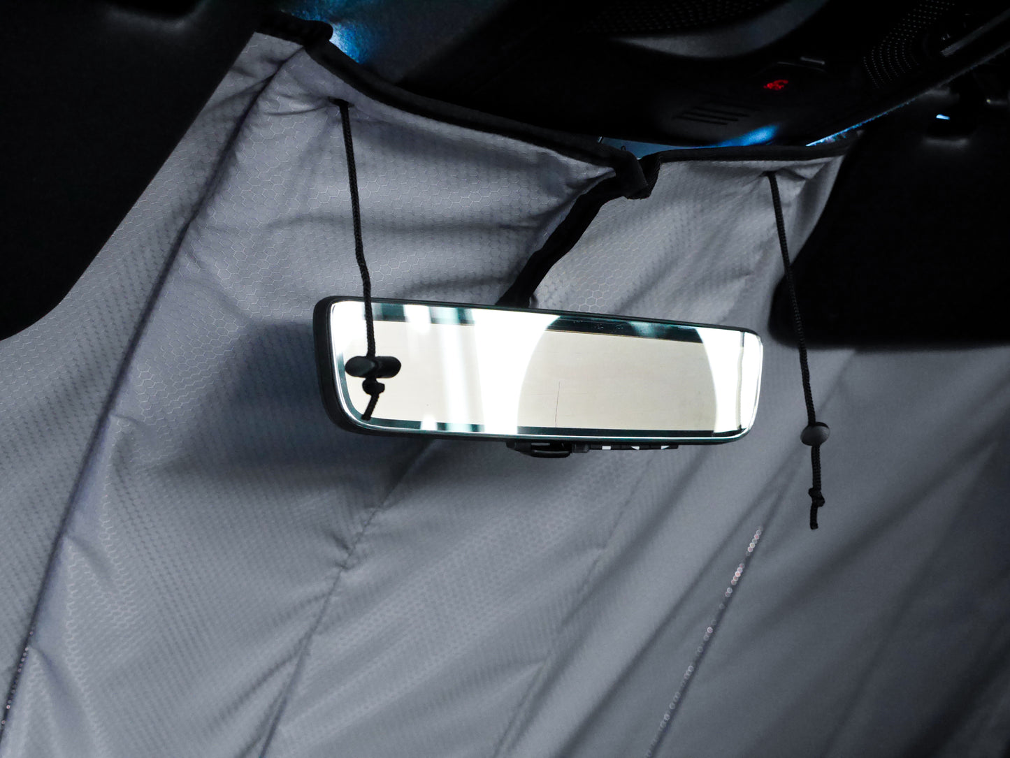 Image showing the window cover for the windshield securely tucked behind the rearview mirror in a Sprinter van, demonstrating a snug and seamless fit.