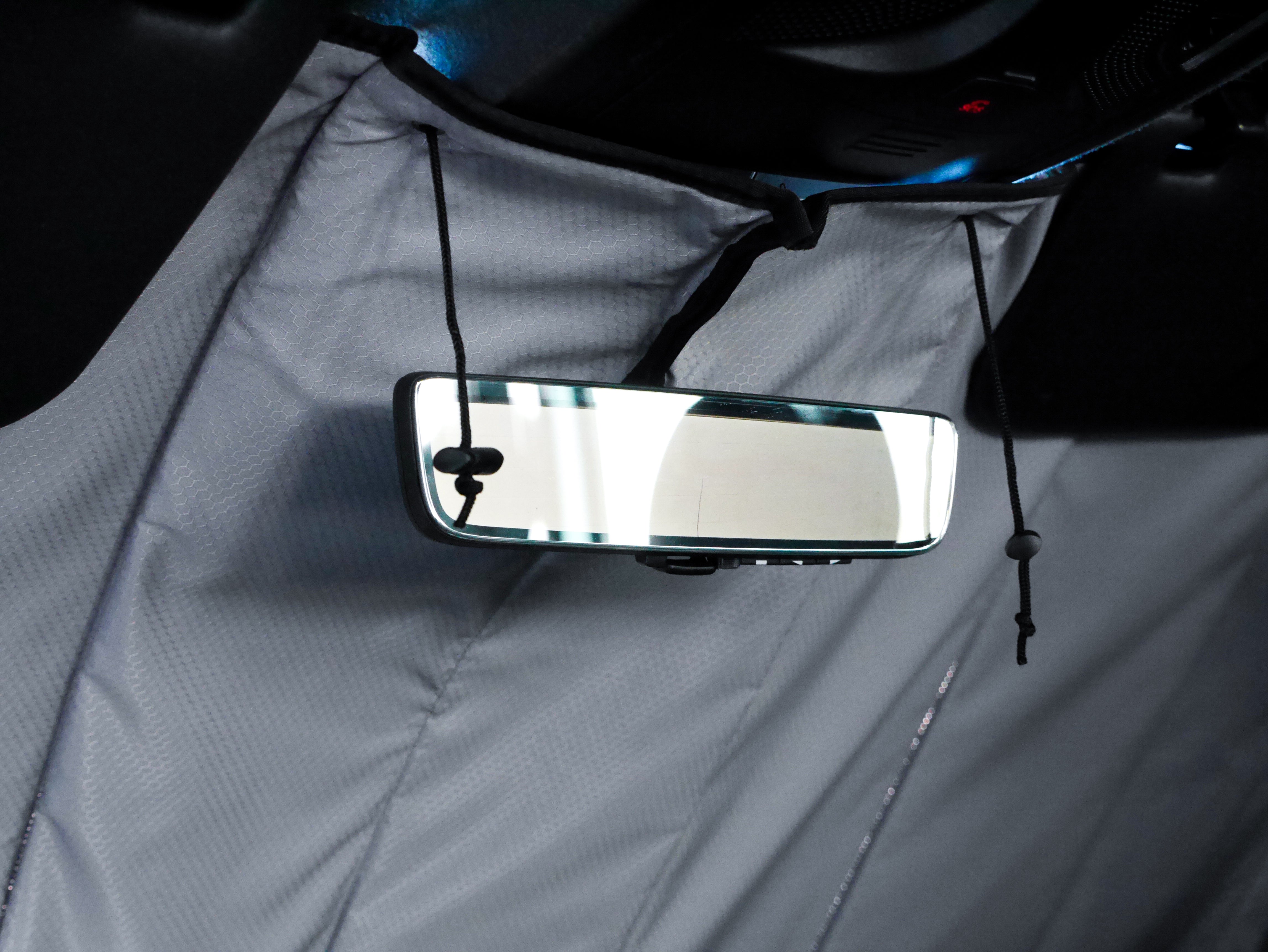 Image showing the window cover for the windshield securely tucked behind the rearview mirror in a Sprinter van, demonstrating a snug and seamless fit.