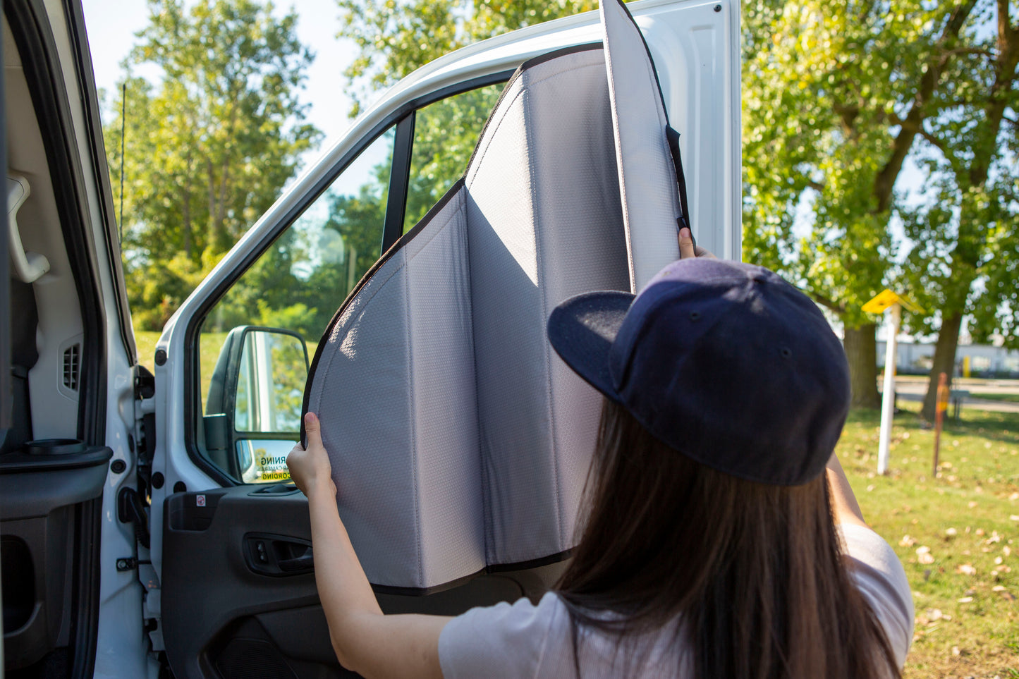 Image of a person attaching a cover to the passenger side window for a Sprinter van, demonstrating the installation process.