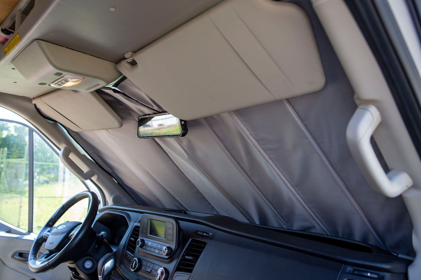 Image showing the window cover for the windshield securely tucked behind the rearview mirror in a camper van, demonstrating a snug and seamless fit.