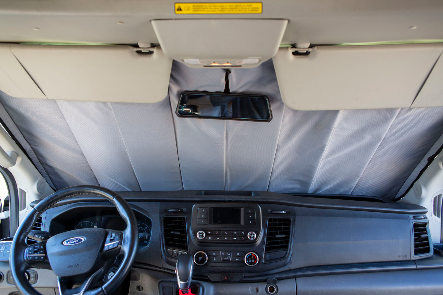 Image showing the window cover for the windshield securely tucked behind the rearview mirror in a camper van, demonstrating a snug and seamless fit.
