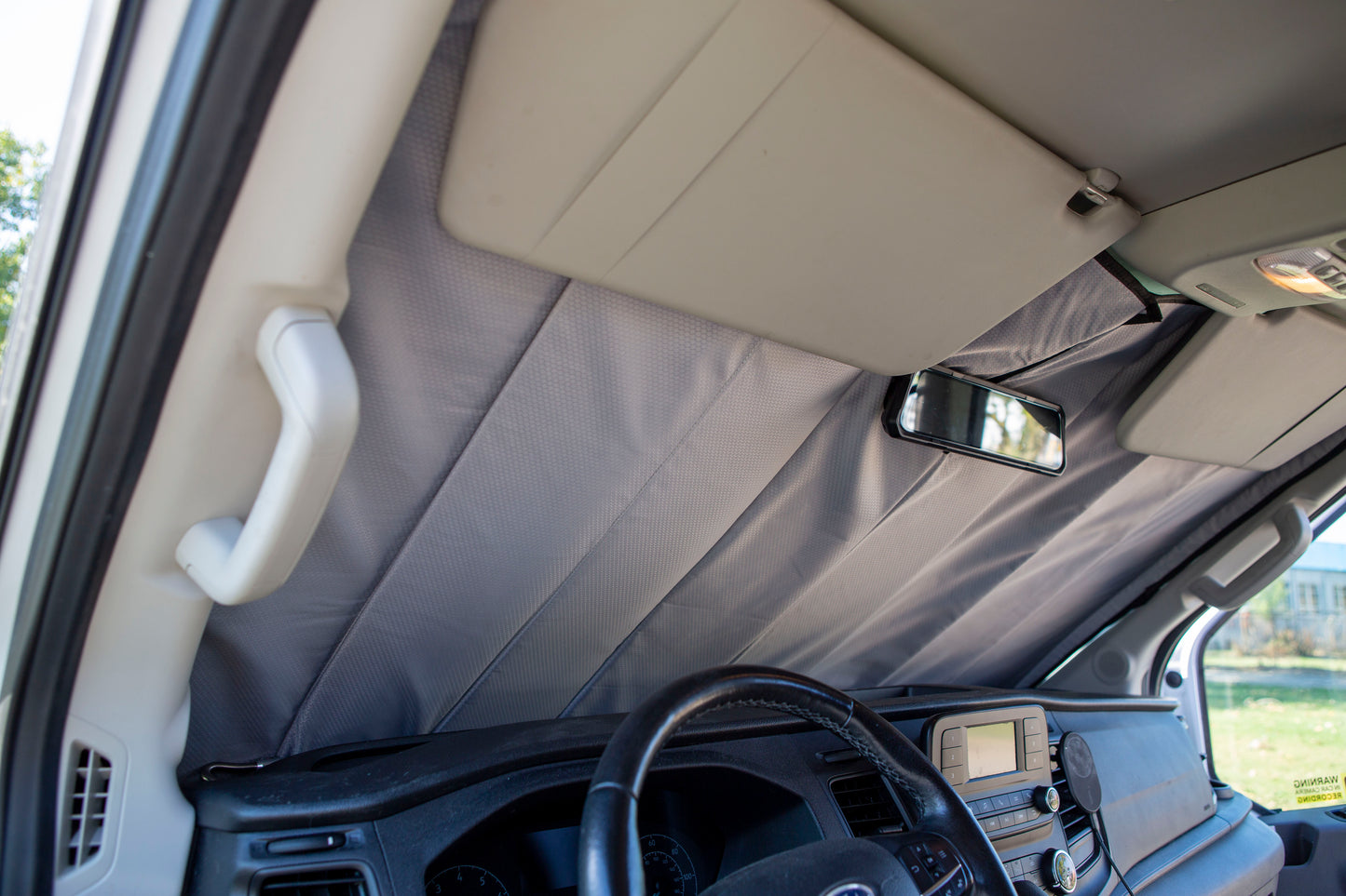 Image showing the window cover for the windshield securely tucked behind the rearview mirror in a camper van, demonstrating a snug and seamless fit.