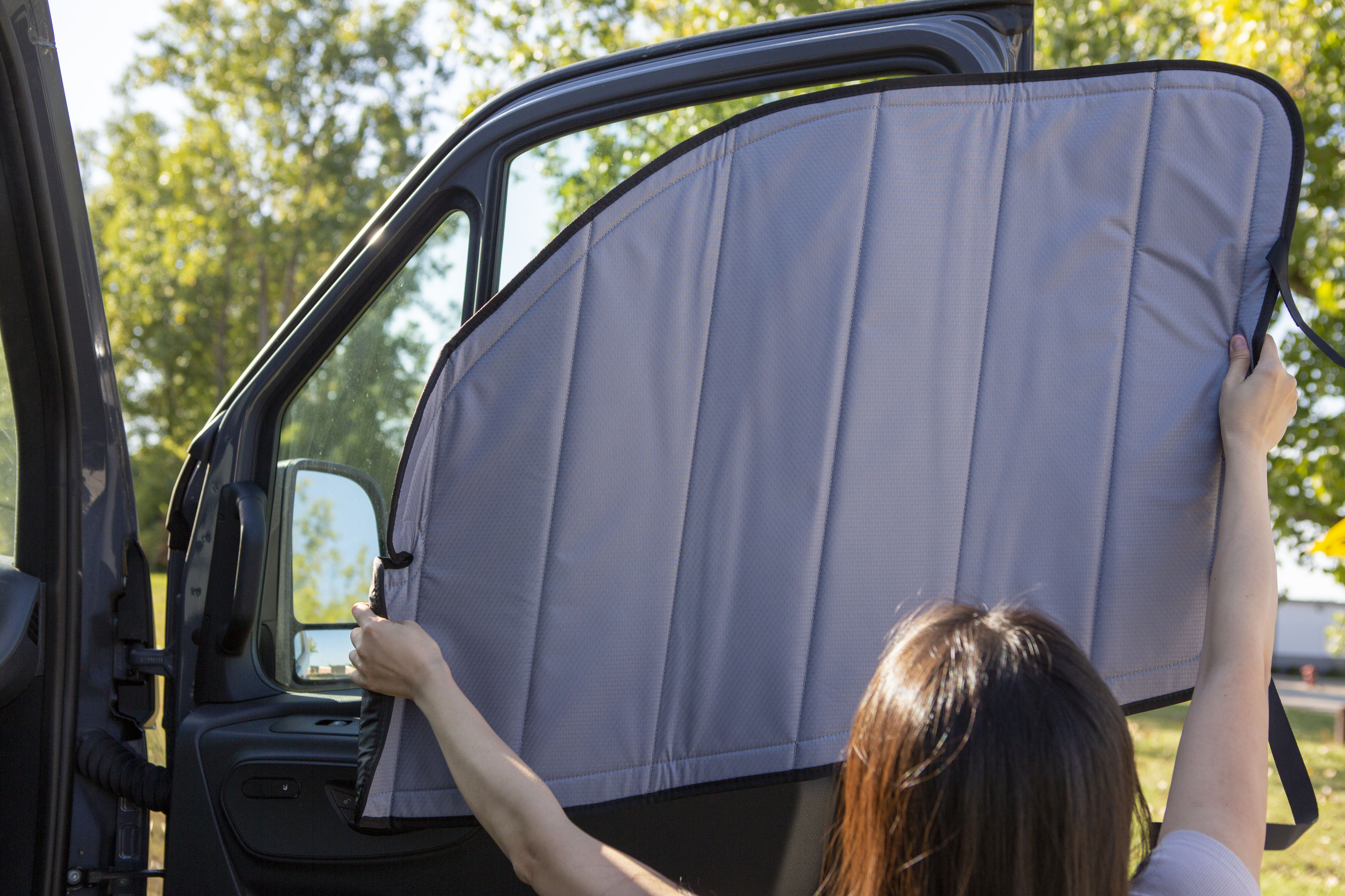 Image of a person attaching a cover to the passenger side window for a Sprinter van, demonstrating the installation process.