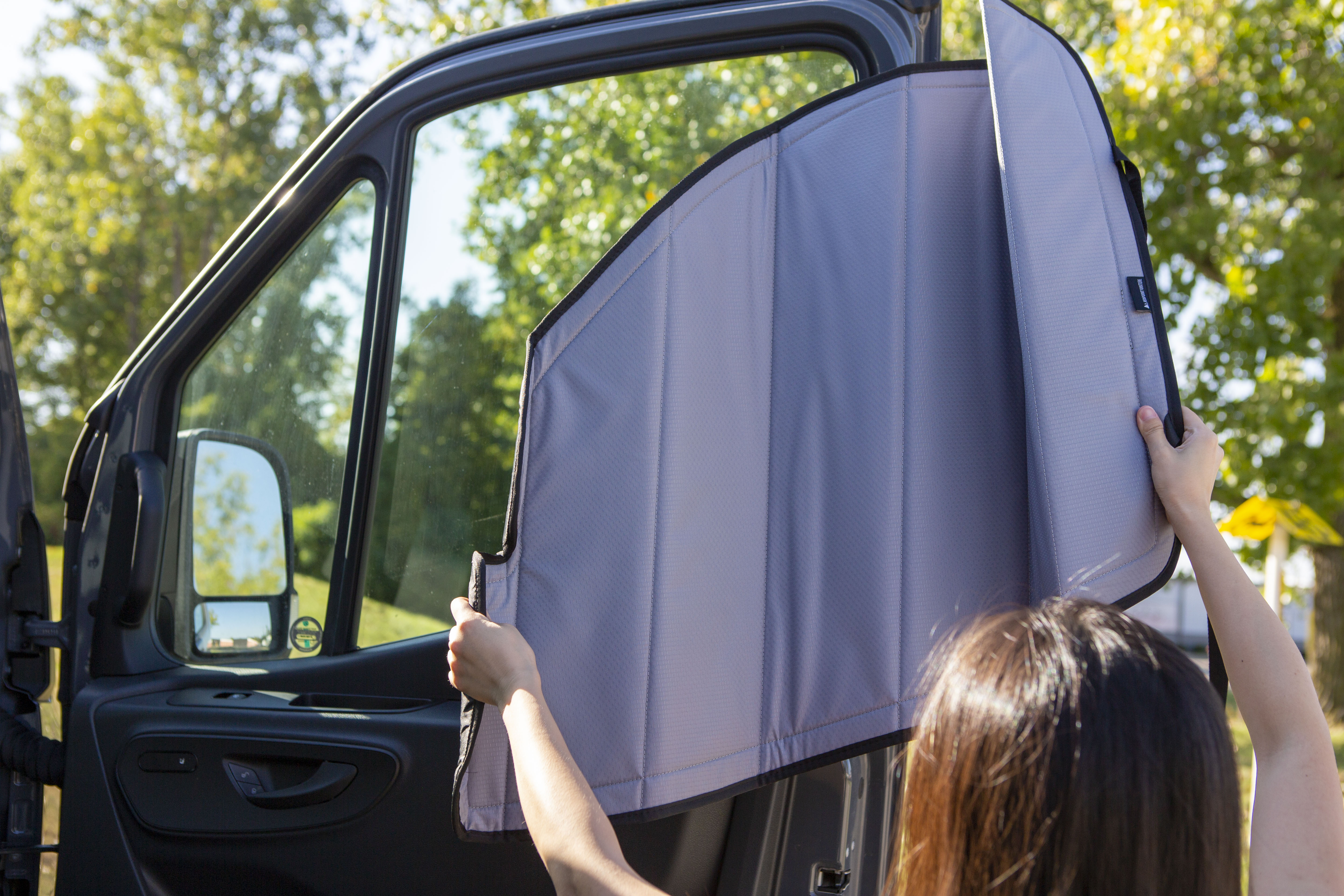 Image of a person attaching a cover to the passenger side window for a Sprinter van, demonstrating the installation process.